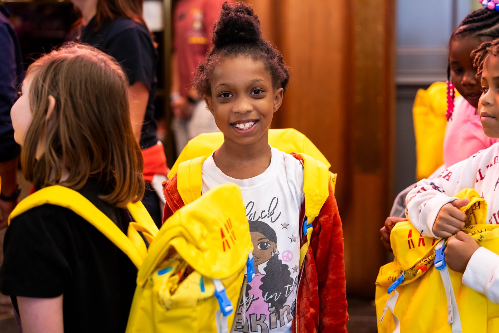 Kids smiling with Aku yellow backpacks at a giveaway
